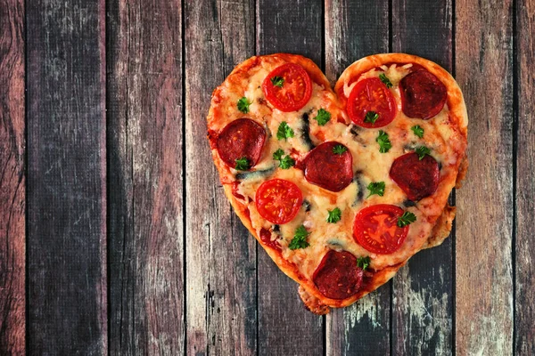 Heart shaped pizza for Valentines Day on a dark wood background. Above view.