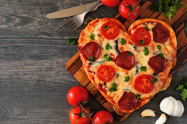 Heart shaped pizza for Valentines Day over a dark wood background. Top view, side orientation. Table scene with ingredients.