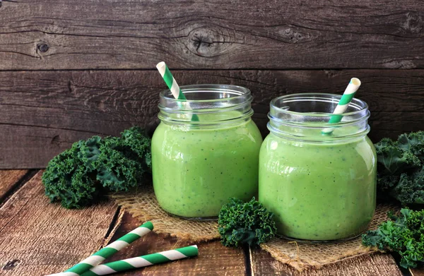 Two green kale smoothies in mason jars. Side view on a rustic dark wood background.