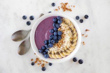Hindistan cevizi, muz, chia tohum ve granola ile sağlıklı blueberry smoothie kase. Düz parlak bir arka plan üzerinde yatıyordu.