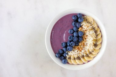 Hindistan cevizi, muz, chia tohum ve granola ile sağlıklı blueberry smoothie kase. Parlak bir arka plan üzerinde üstten görünüm.