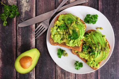 Bütün tahıl ekmeği üzerinde kabak ve Chia tohumları ile avokado tost. Koyu ahşap arka planda görünümü yukarıda.
