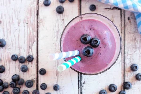 Blueberry smoothie in a glass with berries, top view over a rustic white wood background