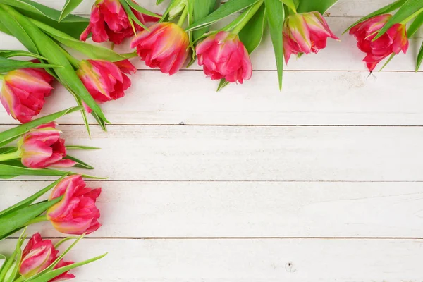 Corner border of pink tulip flowers against a white wood background with copy space