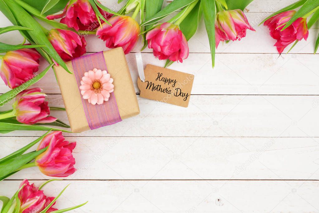 Corner border of pink flowers with Happy Mothers Day gift and tag against a rustic white wood background