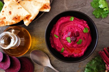 Pancar humus daldırma, koyu arka planda düz ekmek ve malzemelerle üst görünüm masa sahnesi