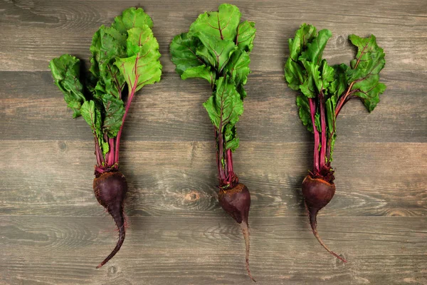 Three individual beetroots with leaves against a rustic wood background