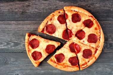 Kesme dilimleri ile geleneksel pepperoni pizza. Ahşap arka planda üst görünüm.