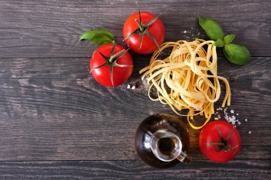 Taze Linguine, domates, zeytinyağı ve fesleğen dahil Makarna malzemeleri. Ahşap arka planda üst görünüm.