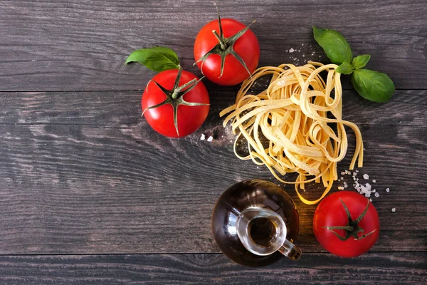 Taze Linguine, domates, zeytinyağı ve fesleğen dahil Makarna malzemeleri. Ahşap arka planda üst görünüm.