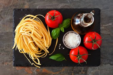 Taze Linguine, domates, zeytinyağı ve fesleğen dahil Makarna malzemeleri. Arduvaz tabağı üzerinde üst görünüm.