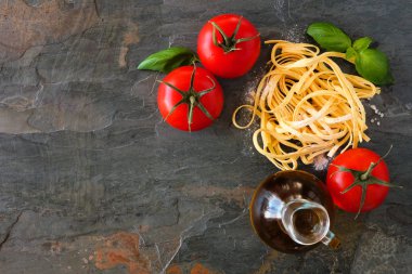 Taze Linguine, domates, zeytinyağı ve fesleğen dahil Makarna malzemeleri. Arduvaz arka planına karşı üst görünüm.