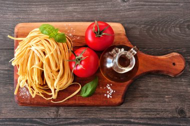 Taze Linguine, domates, zeytinyağı ve fesleğen dahil Makarna malzemeleri. Ahşap tabakta üst görünüm.