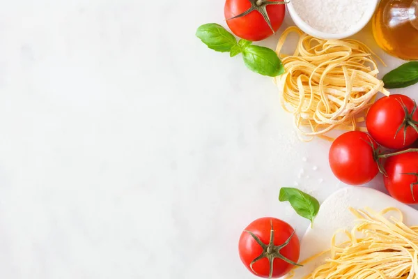 Pasta ingredients including fresh linguine, tomatoes, olive oil and basil. Above view, side border against a white marble background. Copy space.