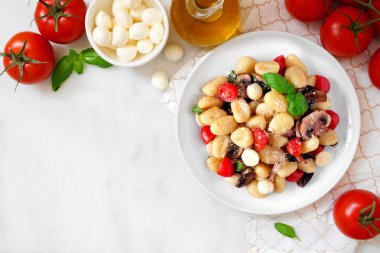 Domates, mozzarella, mantar ve fesleğen ile Gnocchi. Kopya alanı ile beyaz mermer arka plan üzerinde üst görünüm köşe sınırı.