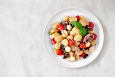 Domates, mozzarella, mantar ve fesleğen ile Gnocchi. Beyaz mermer arka plan üzerinde üst görünüm.