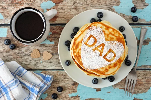 Fathers Day pancakes with heart shape and DAD letters. Fathers Day breakfast concept. Top view on a rustic blue wood background.