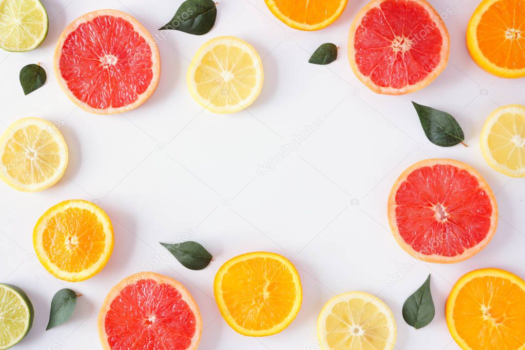 Colorful fruit frame of fresh citrus slices with leaves. Top view, flat lay over a white background with copy space.
