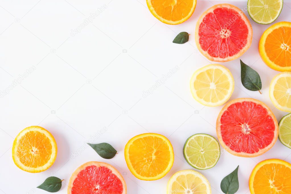 Colorful fruit corner border of fresh citrus slices with leaves. Top view, flat lay over a white background with copy space.