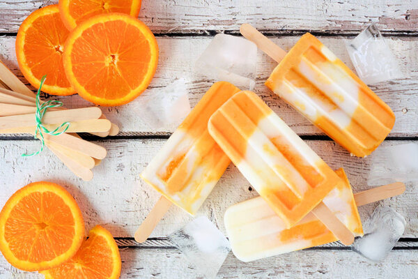 Апельсиновый йогурт эскимо, вид сверху стол сцены разбросаны на белом фоне дерева
