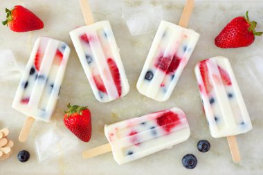 Sağlıklı çilek yaban mersini yaz yoğurt popsicles, üst görünümü beyaz mermer arka plan üzerinde dağınık