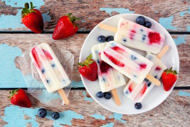 Bir tabakta sağlıklı çilek yaban mersini yoğurt popsicles, mavi ahşap arka plan karşı üst görünüm yaz masa sahnesi