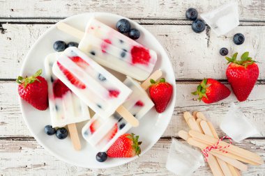Sağlıklı çilek yaban mersini yoğurt bir tabakta popsicles, beyaz ahşap arka plan karşı üst görünüm yaz masa sahnesi