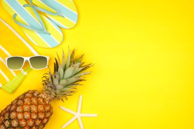 Sarı arka planda plaj aksesuarları. Kopya alanı ile Yaz tatili kavramı yan sınır. Güneş gözlüğü, denizyıldızı, havlu, parmak arası terlik ve ananas.