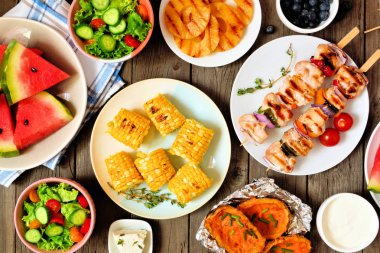 Yaz Barbekü veya piknik gıda kavramı. Meyve, salata, ızgara et ve patates seçimi. Rustik ahşap arka plan üzerinde havai masa sahnesi.