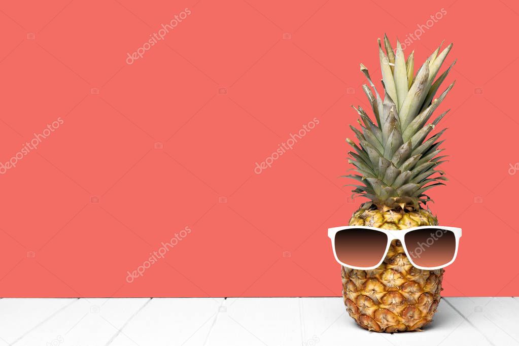 Hipster pineapple with sunglasses against a living coral colored background. Minimal summer concept.