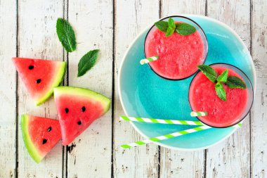 Mavi servis plakasında iki bardakta karpuz suyu. Beyaz ahşap arka planda üst görünüm.