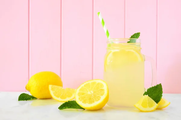 Homemade lemonade in a mason jar glass with lemons. Side view on a pastel pink wood background.