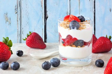 Bir rustik mavi ahşap arka plan karşı bir bardak çilek ve yaban mersini parfait