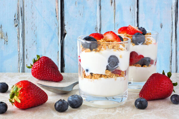 Strawberry and blueberry parfaits in glasses against a rustic blue wood background