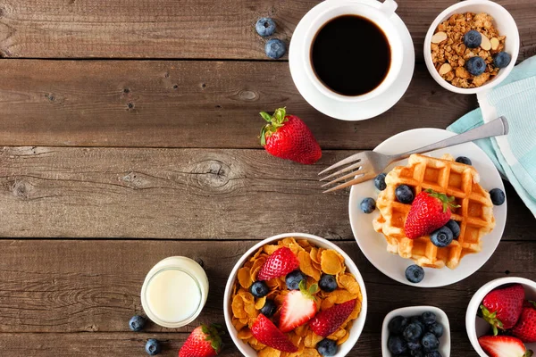 Breakfast food corner border. Fruits, cereal, waffles, milk and coffee. Top view over a dark wood background with copy space.