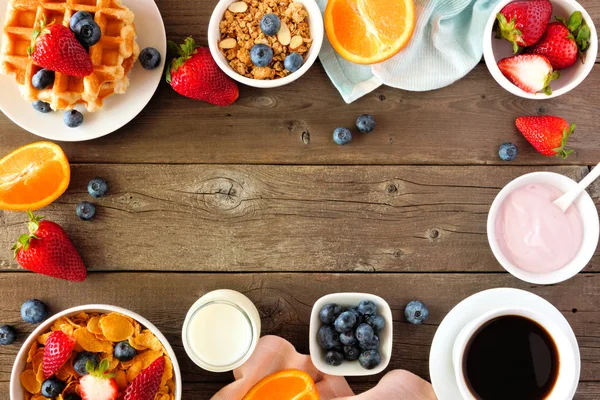 Breakfast food frame. Fruits, cereal, waffles, yogurt, milk and coffee. Top view over a dark wood background with copy space.