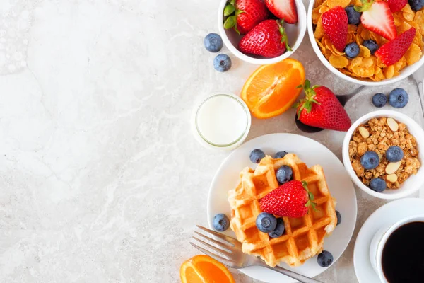 Breakfast food side border. Fruits, cereal, waffles, coffee and milk. Top view over a bright stone background with copy space.