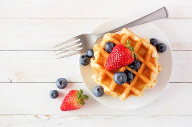 Çilek ve yaban mersini ile kahvaltı waffle. Beyaz ahşap arka plan üzerinde üst görünüm.