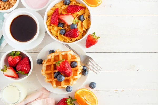 Breakfast food side border. Fruits, cereal, waffles, milk and coffee. Top view over a white wood background with copy space.