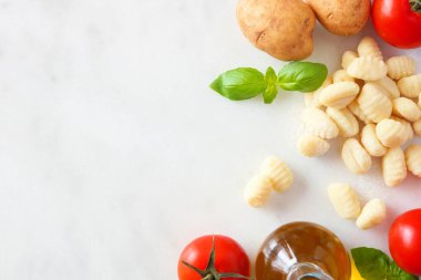 Taze gnocchi, domates, zeytinyağı, patates ve fesleğen dahil Gnocchi Yemek malzemeleri. Üst görünüm, beyaz mermer arka planda yan sınır. Boşluk Kopyala.
