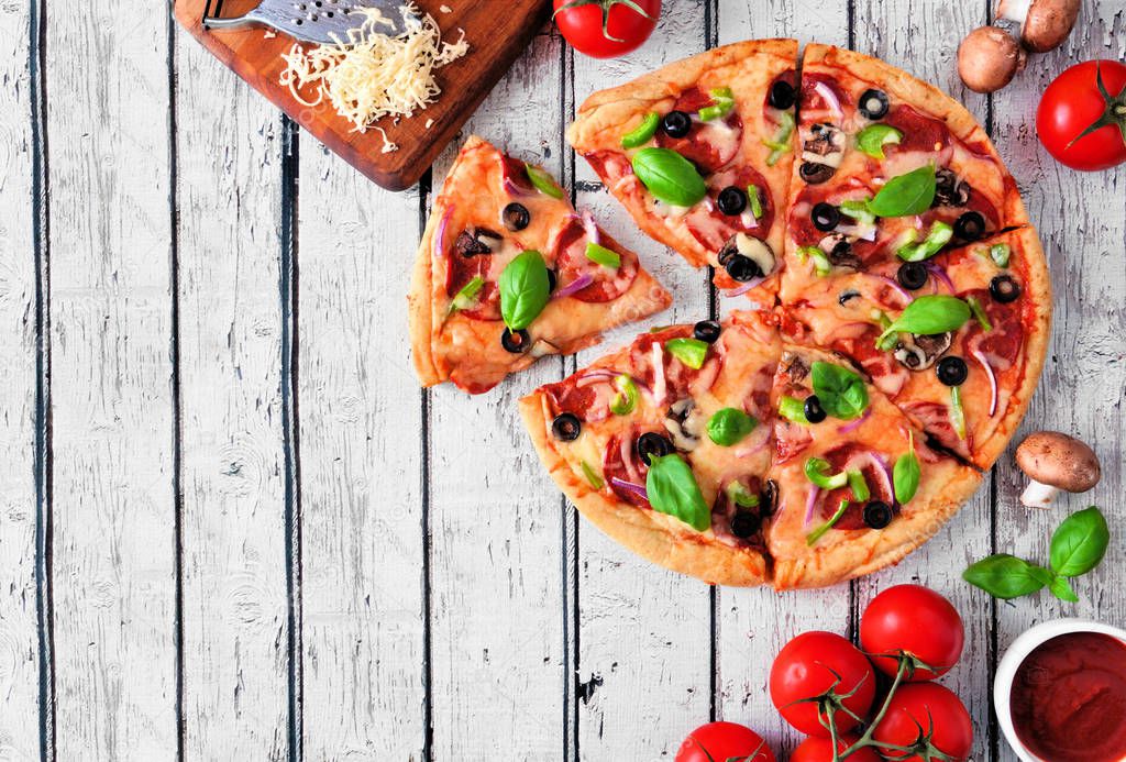 Homemade pizza with pepperoni, mushrooms, green peppers, olives, onions and basil. Top view, corner border against a white wood background with copy space.