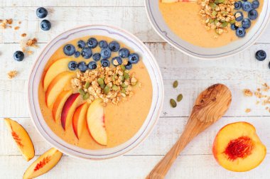 Yaban mersini ve granola ile sağlıklı şeftali smoothie kase. Beyaz ahşap arka planile üst görünüm masa sahnesi.