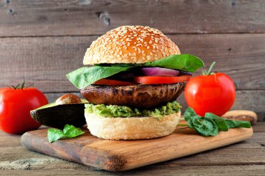 Koyu ahşap arka plan karşı ahşap servis tahtası üzerinde avokado, domates, ıspanak ve soğan ile Portobello mantar vegan burger