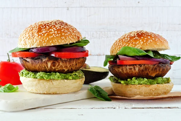 Portobello mushroom vegetarian burgers with avocado, tomato, spinach and onion against a white wood background