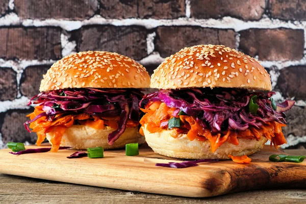 Pulled carrot meatless burgers with red cabbage slaw against a dark brick background. Healthy eating, plant-based meat substitute concept.