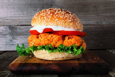 Koyu ahşap arka plan karşı bir servis tahtası üzerinde buffalo soslu karnabahar burger. Sağlıklı beslenme, bitki bazlı et ikame konsepti.
