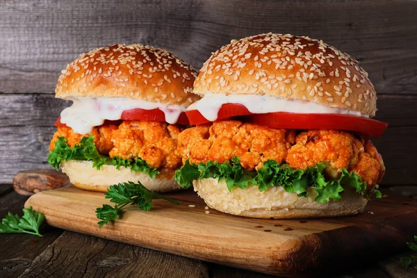 Bir ahşap arka plan karşı bir servis tahtası üzerinde buffalo soslu karnabahar burger. Sağlıklı beslenme, bitki bazlı et ikame konsepti.