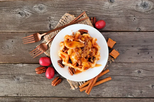 Fırında elma, pekan ve karamel ile tatlı kahvaltı waffle. Malzemelerin çerçeve ile rustik ahşap arka plan üzerinde üst görünümü. Sonbahar gıda teması.