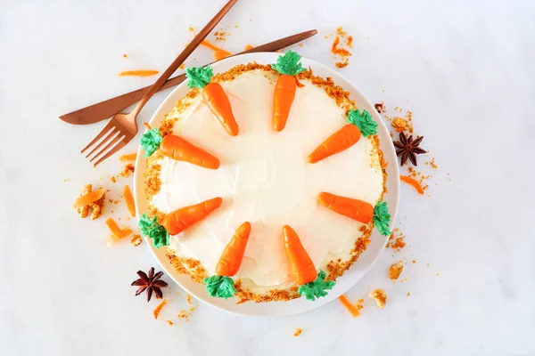Homemade carrot cake with cream cheese frosting and fondant carrots. Top view over a white marble background.
