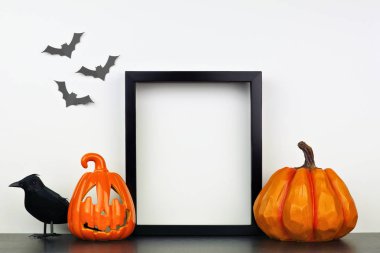 Jack o Lantern, balkabağı ve karga dekoru ile bir raf veya masada siyah çerçeve kadar mock. Cadılar Bayramı konsepti. Yarasalarla beyaz bir duvara karşı portre çerçevesi.